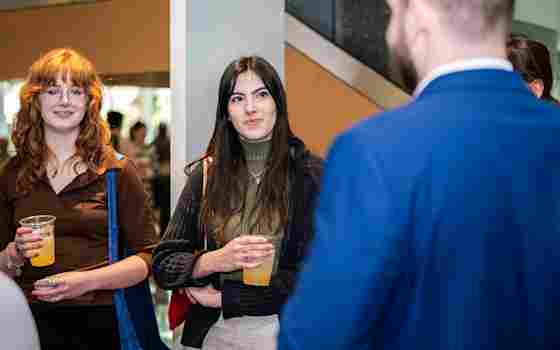 Two guests holding drinks and speaking to an event speaker in a blue suit, during a reception inside Center for BrainHealth's spacious and modern Brain Performance Institute.