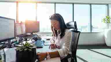 Businesswoman sitting in her brightly-lit office and working on paperwork at her desk.