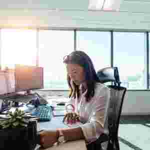 Businesswoman sitting in her brightly-lit office and working on paperwork at her desk.