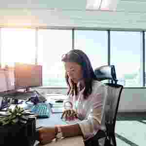 Businesswoman sitting in her brightly-lit office and working on paperwork at her desk.