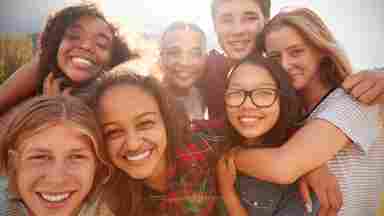 Several young people of various ganders and races smile as their picture is taken; they are crowded closely together.