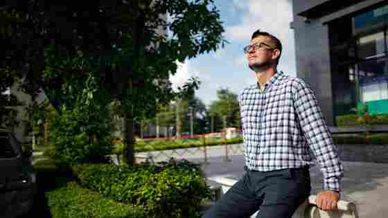 A young professional in plaid shirt gazes across the lawn outside an off building, taking a break in some brain-healthy sunshine.