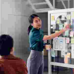 Asian UX developer and UI designer presenting a design for a mobile app interface on a whiteboard at a meeting.