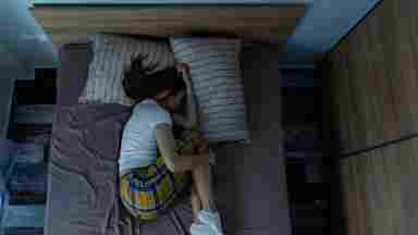 A college student sleeps soundly in fetal position as morning light comes in the window.