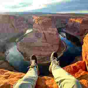 A young adult rests besides the Grand Canyon taking in the expansive perspective of the landscape.