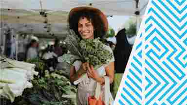 A young gardener wearing a sunhat and smiling with a large bouquet of fresh, green kale.