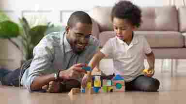 A happy father is playing blocks with his son on the wooden floor.