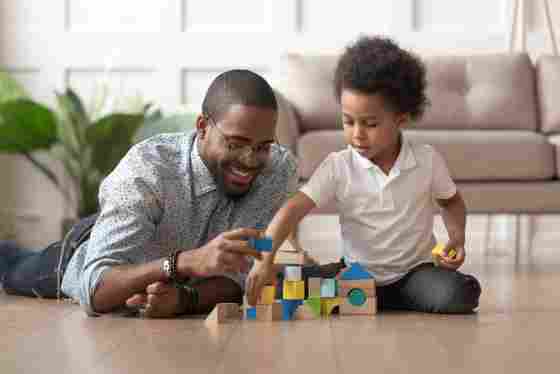 A happy father is playing blocks with his son on the wooden floor. 