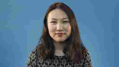 A headshot of Dr. Xiaosi Gu, assistant professor in the School of Behavioral and Brain Sciences at UTD. She wears a dark, patterned top and stands in front of a blue background.