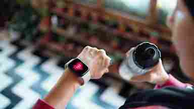 Person wearing smartwatch displaying heart rate of 143 while holding water bottle during workout.