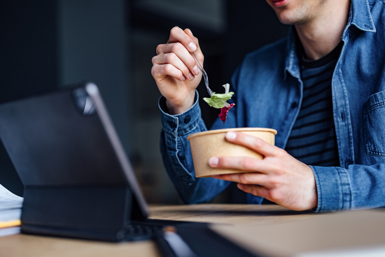 A college student studying on their laptop while eating a healthy lunch. 