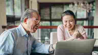 Happy, senior Asian couple using laptop at home together.