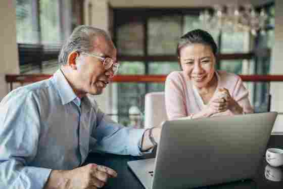 Happy, senior Asian couple using laptop at home together.