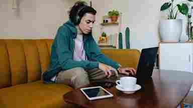 Young adult wearing a headset and working on a laptop.