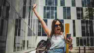 Joyous college student standing outside campus buildings as she looks at her grades.