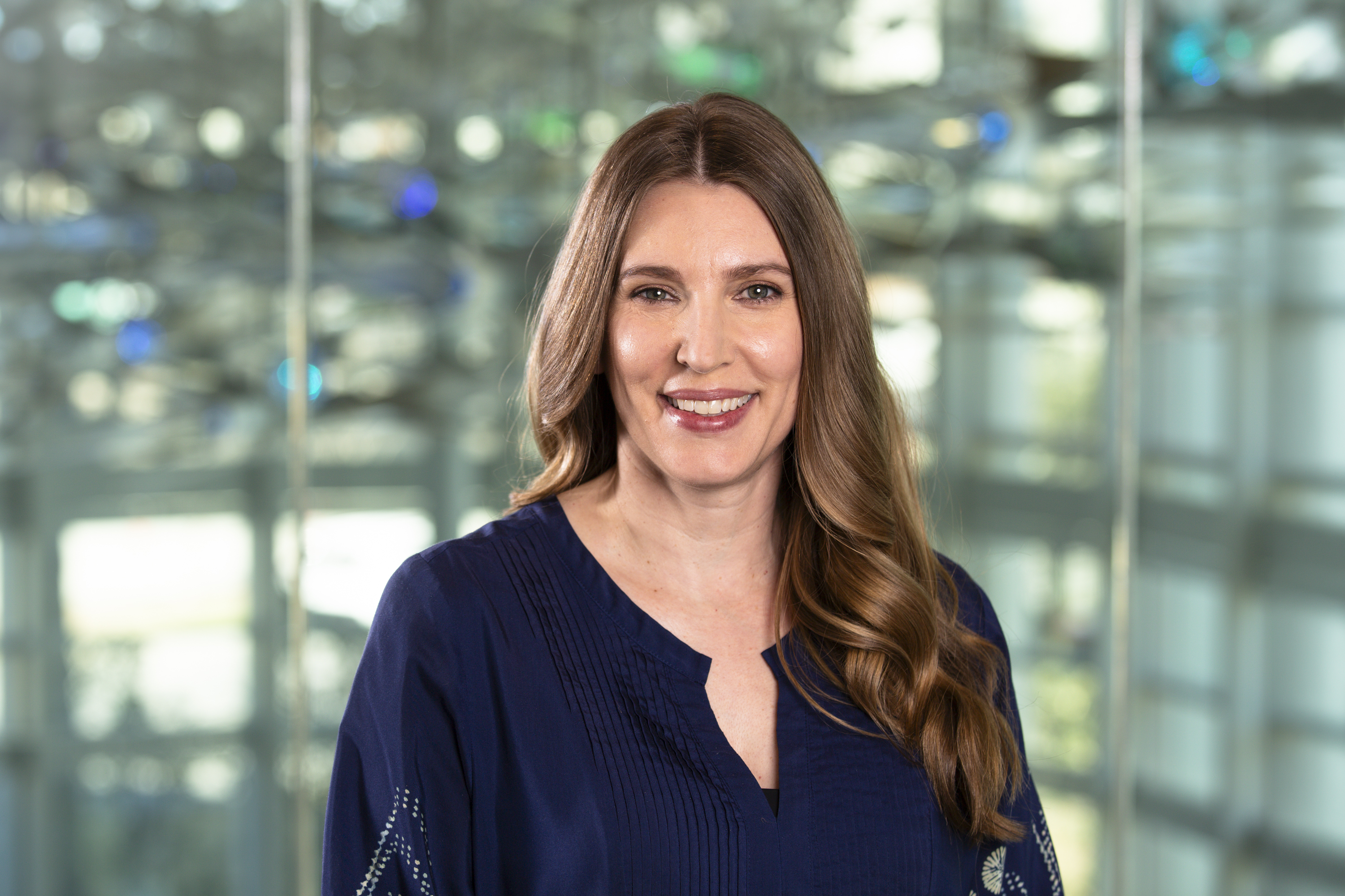Rebecca Fisher's headshot, pictured in front of a a large, luminescent sculpture of neurons at Center for BrainHealth.