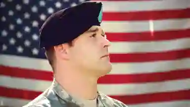 A man in military uniform stands in front of the American flag