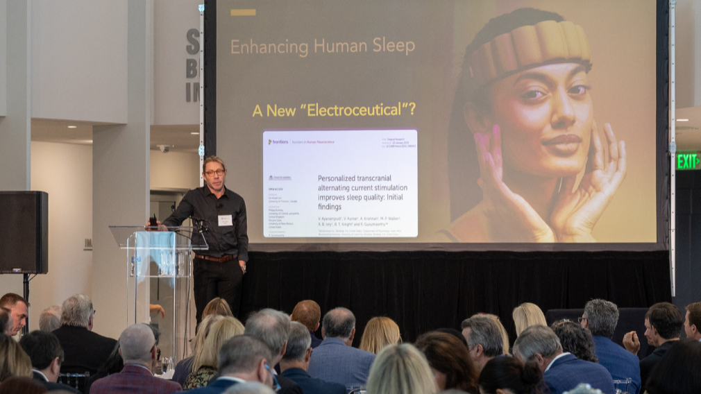 Sleep expert and neuroscientist Dr. Matt Walker speaks at BrainHealth Week in Dallas, Texas, shown delivering a TEDx-style talk during a large conference event.