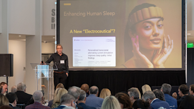 Sleep expert and neuroscientist Dr. Matt Walker speaks at BrainHealth Week in Dallas, Texas, shown delivering a TEDx-style talk during a large conference event.