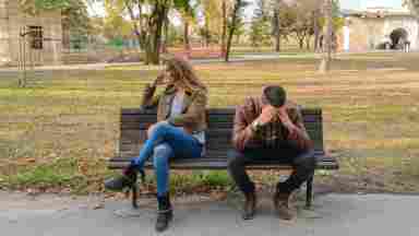 Woman and man sitting on a park bench, fustrated with each other