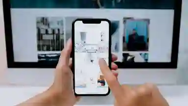 A person's phone open to Instagram looking at images while a laptop is out of focus in the background