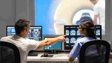 Researchers analyze MRI scan results, while a study participant receives a scan in the background.