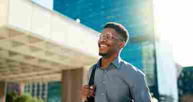 A man walking outside and smiling in the sun. He is dressed in office attire.