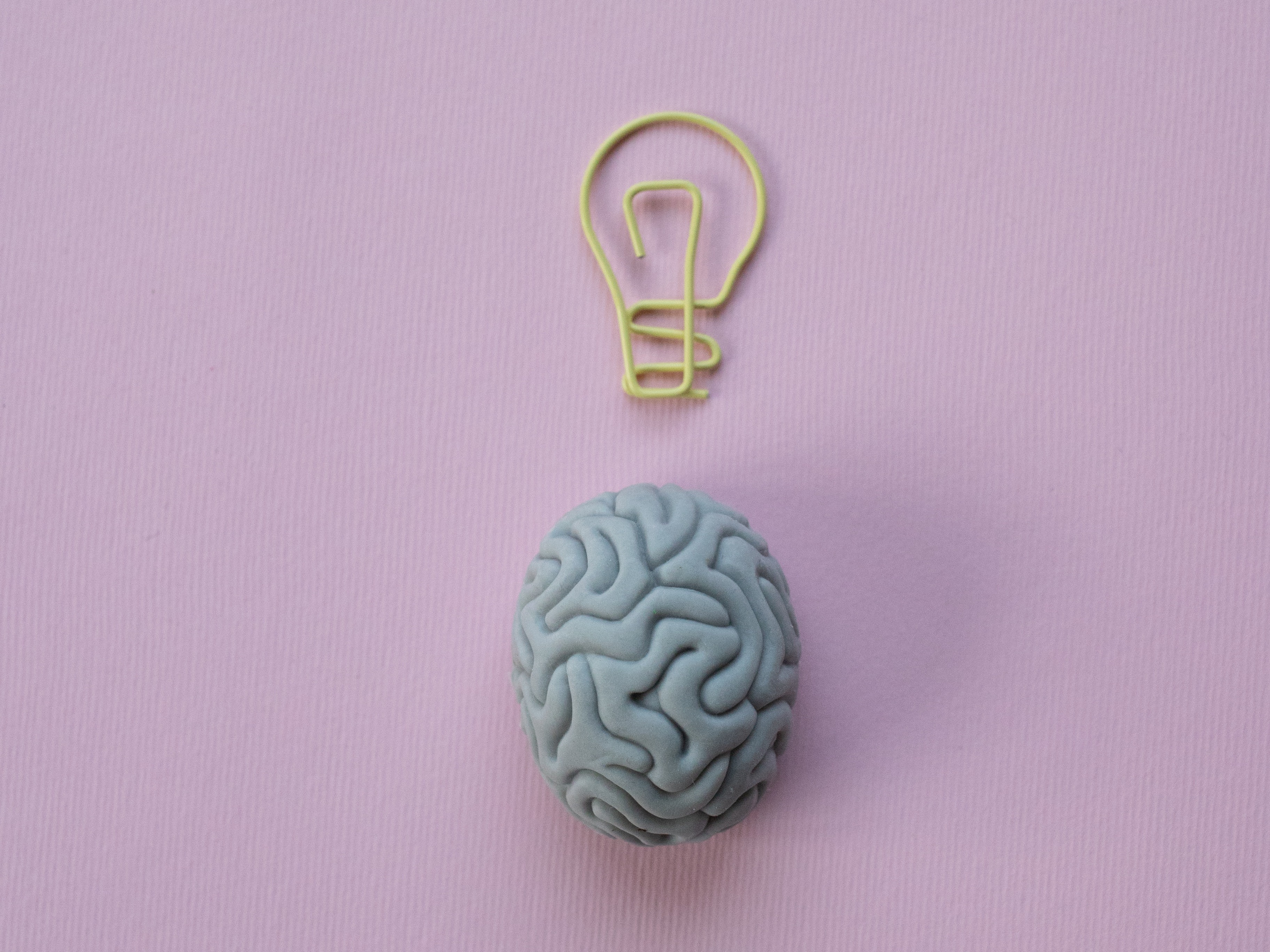 Yellow paper clip in the form of a light bulb on a pink background above a gray eraser that looks like a brain