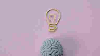 Yellow paper clip in the form of a light bulb on a pink background above a gray eraser that looks like a brain