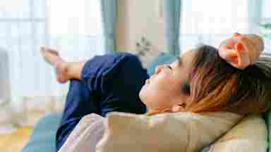 A young Asian woman lying down on a sofa and resting in a living room.