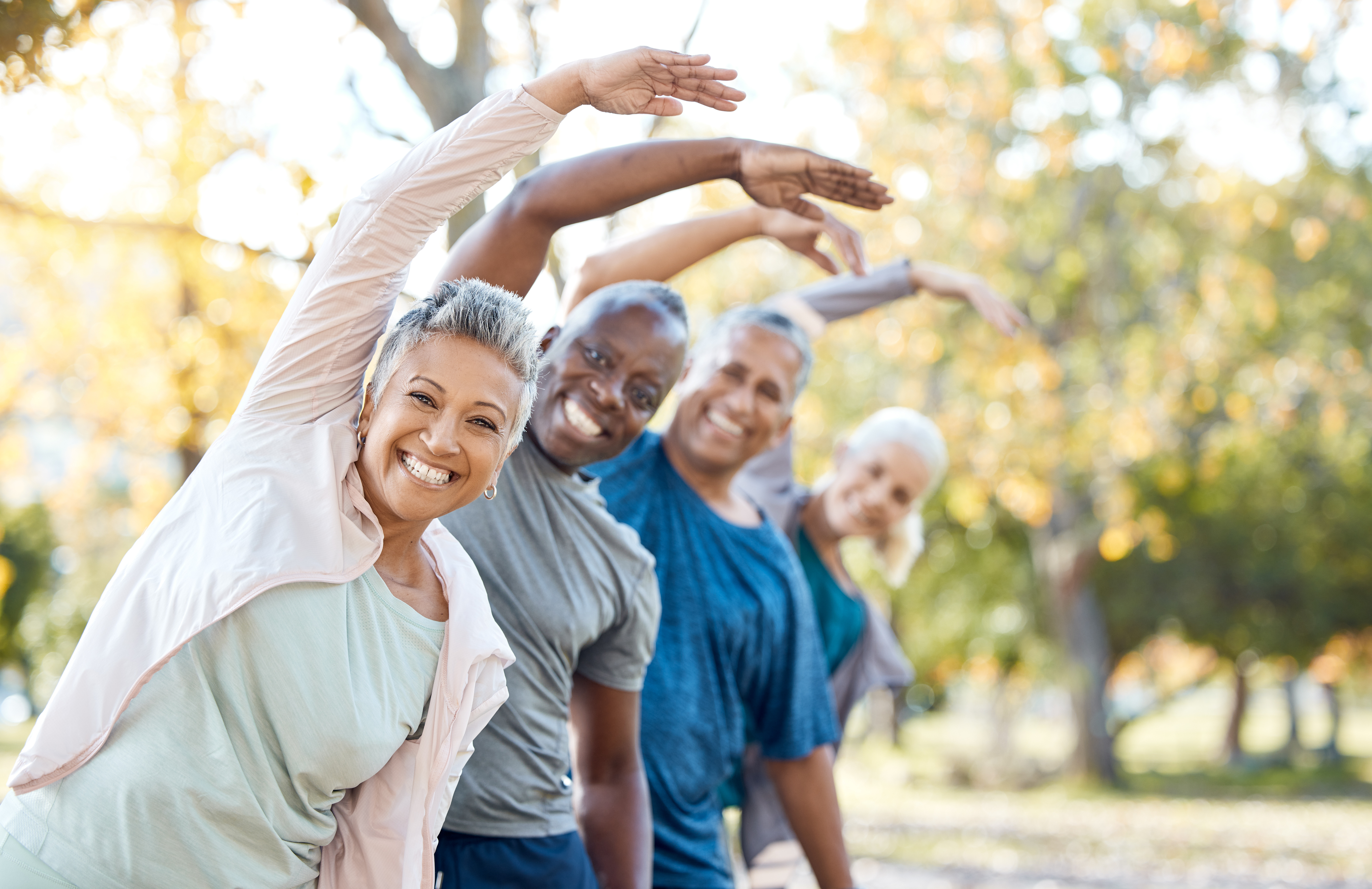 Mature friends of color enjoy group exercise at a park. 