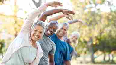 Mature friends of color enjoy group exercise at a park.