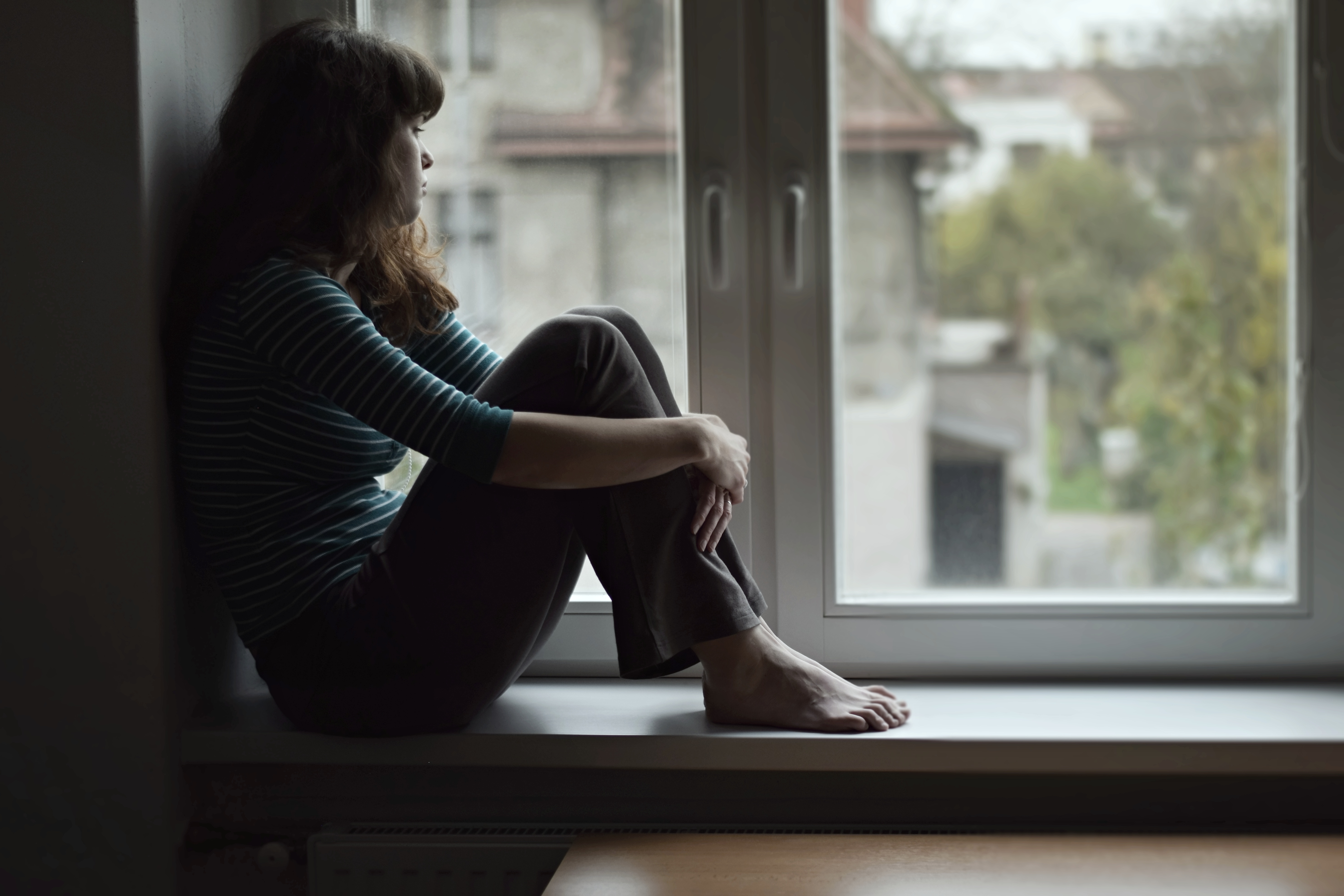 A young woman sitting alone and staring out of a window.