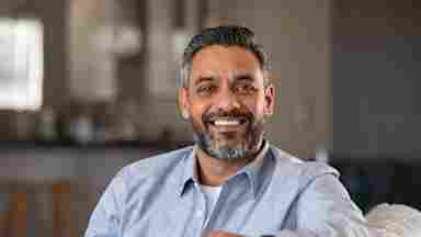 A happy man is smiling into the camera on the couch.