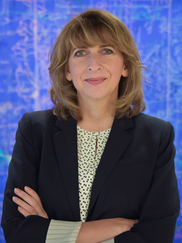 A headshot of Leanne Young, M.A. against a blue backdrop. She has her arms crossed and is wearing a dark blazer with a light blouse underneath.