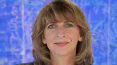 A headshot of Leanne Young, M.A. against a blue backdrop. She has her arms crossed and is wearing a dark blazer with a light blouse underneath.