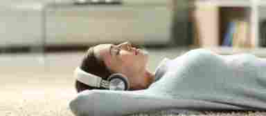 Woman reclining on white carpet, relaxing and listening with headphones.