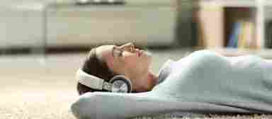 Woman reclining on white carpet, relaxing and listening with headphones.