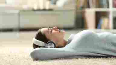 Woman reclining on white carpet, relaxing and listening with headphones.