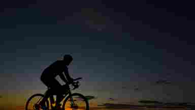 Silhouette of bicycle rider moving through an open area during sunset.