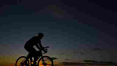 Silhouette of bicycle rider moving through an open area during sunset.