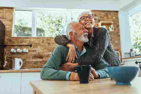 A happy elderly couple is hugging in the kitchen. 