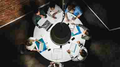 Overhead view of colleagues sharing and analyzing reports at a round table.