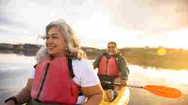 A mature Latino couple happily kayak together and watch a glowing sunset.