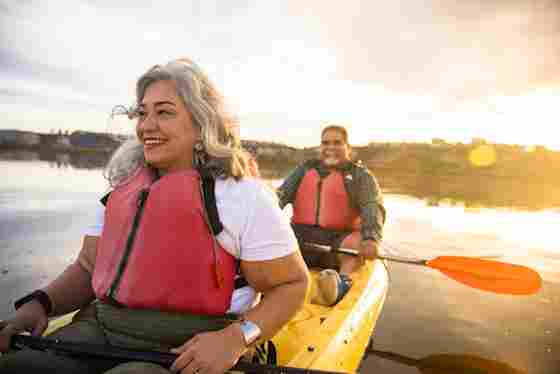 A mature Latino couple happily kayak together and watch a glowing sunset.