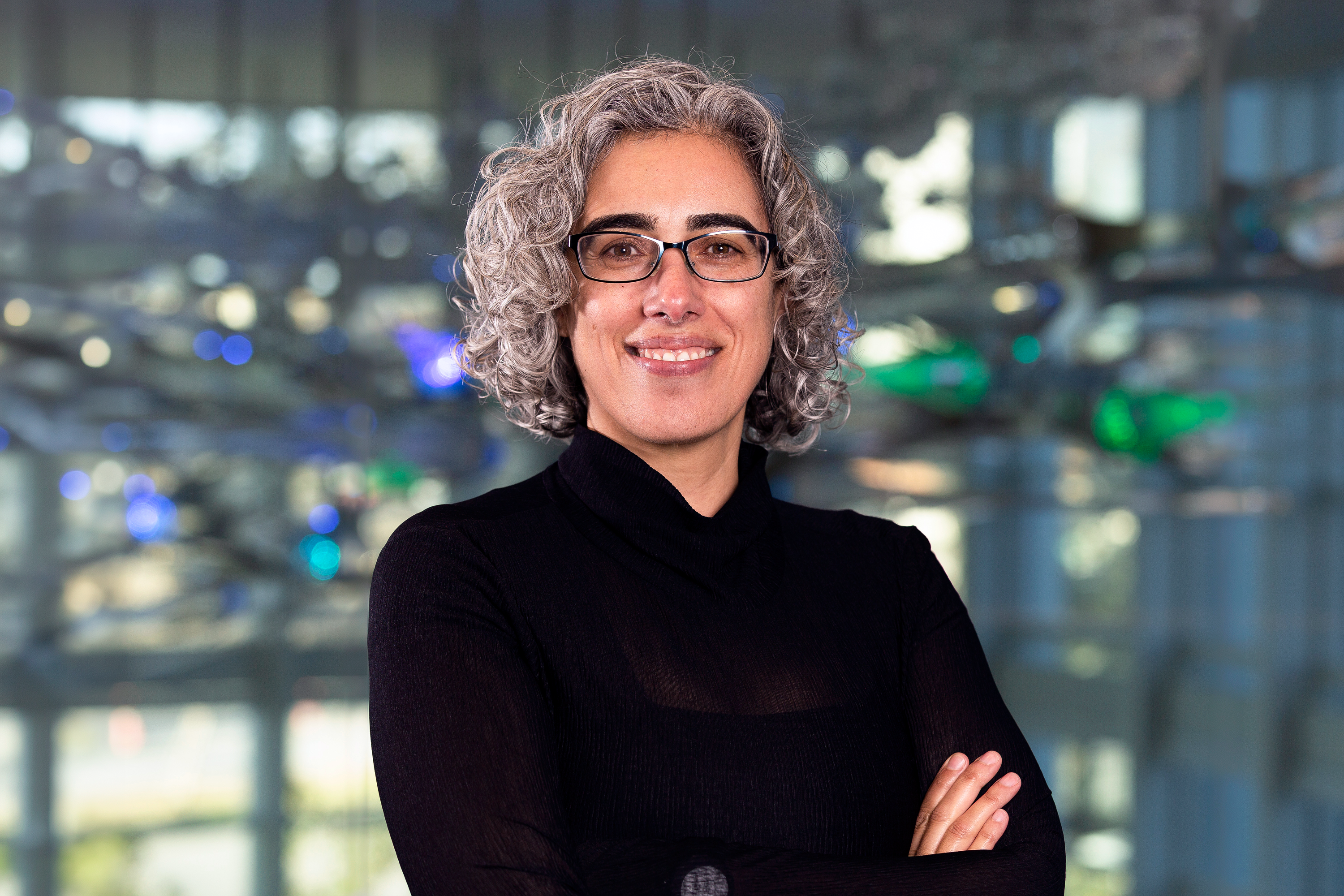 Photograph of neuroscientist Eti Ben Simon, PhD at Center for BrainHealth in Dallas, Texas, with a luminous glass sculpture of human neurons in the background.
