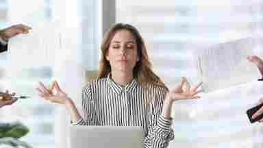 Female executive meditates in front of laptop as people bring her paperwork. 