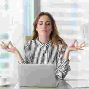 Female executive meditates in front of laptop as people bring her paperwork. 