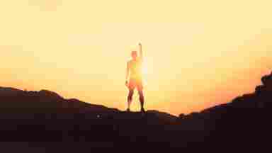 Athlete on top of mountain at sunset, triumphantly raising their fist to the sky.