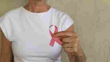 Woman in white t-shirt holding pink breast cancer awareness ribbon in her hand to promote prevention and women's health. 